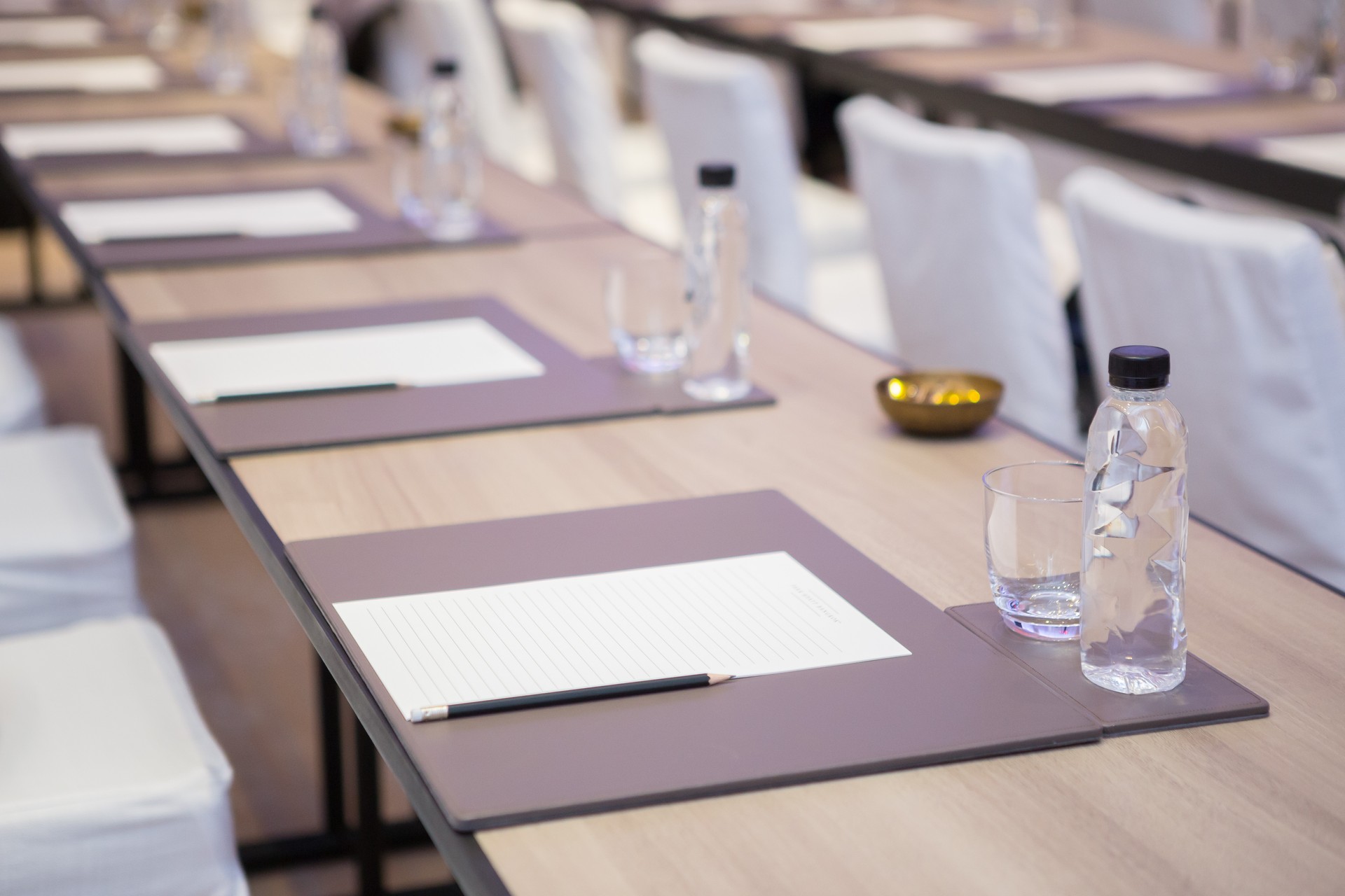 Paper, pencil, water bottle, glass on the table in the seminar room background